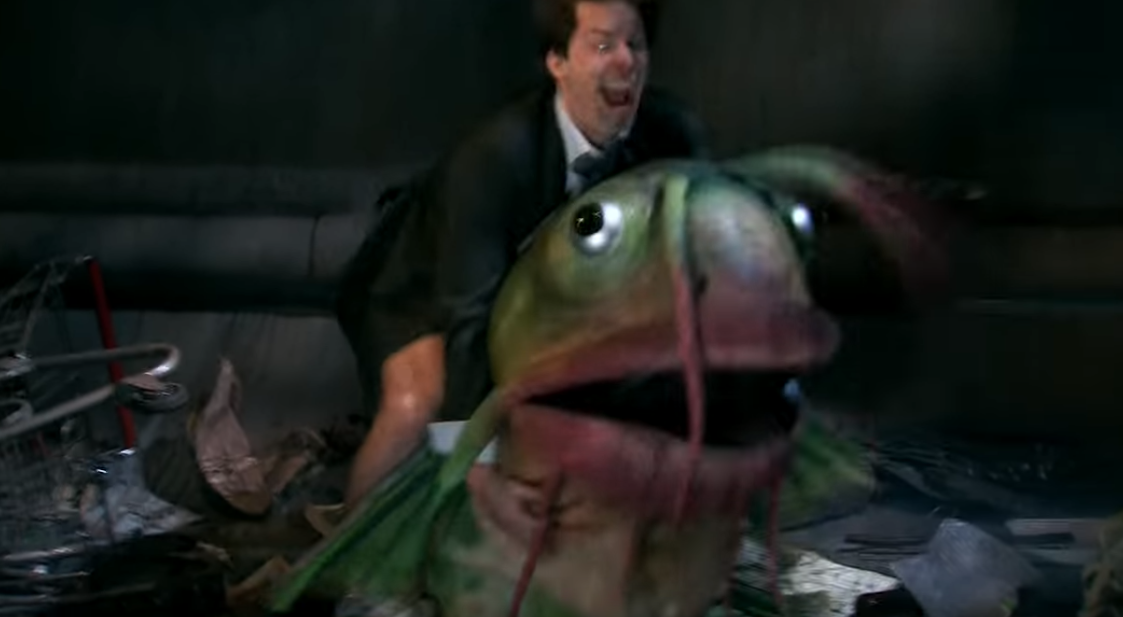 Personagem do Andy Samberg, vestido de roupa social, sarrando um peixe gigante por trás.